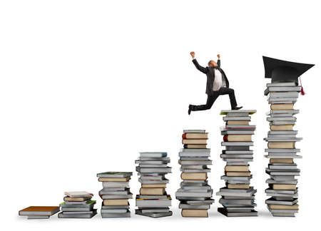 Business man reaches the graduation hat jumping on piles of books. Concept of success and...