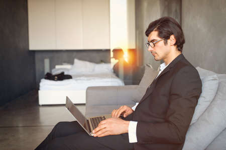 Young businessman sitting on the floor while working from home with a laptopの写真素材