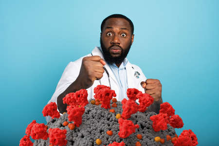 Worried medic is attacked by covid-19 coronavirus. Blue background