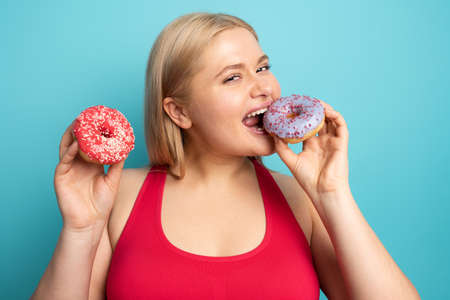 Fat girl eats sweet instead of do gym. Cyan backgroundの写真素材
