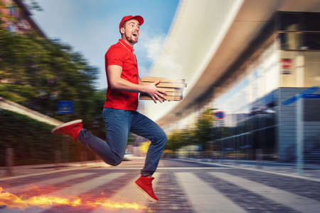 Messenger in red uniform runs on foot really fast to deliver quickly hot pizzas just bakedの写真素材