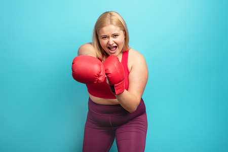 Fat girl in fitness suite does boxing. Cyan background