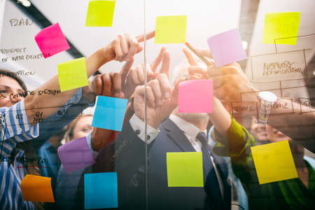 Team of people at work in the office indicates with their hand a post-it on the glassの写真素材