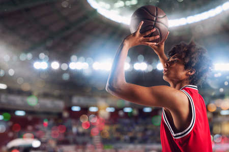 Basketball player throws the ball in the basket in the stadium full of spectators.