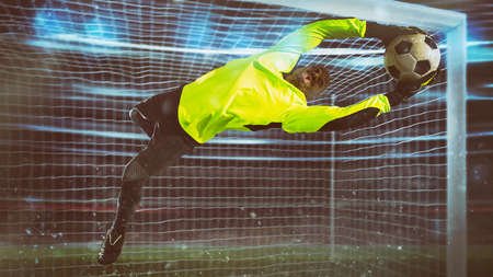 Soccer goalkeeper, in fluorescent uniform, makes a save and avoids a goal during a night matchの写真素材