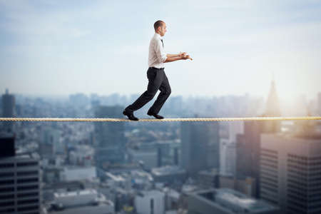 Worry man in balance walking on a rope over a cityの写真素材
