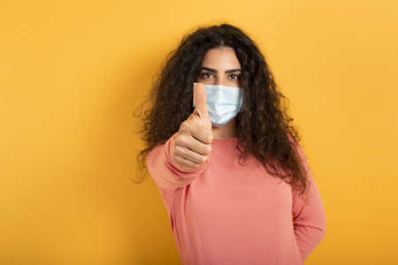 Girl is optimistic about the defeat of covid 19 coronavirus. yellow background.の写真素材