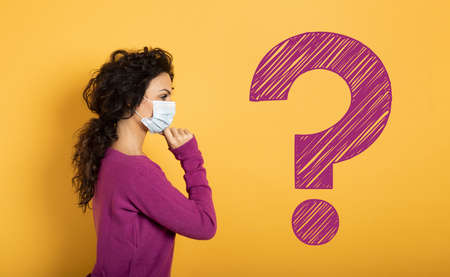 Girl with face mask has a lot of question about covid 19. Yellow backgroundの写真素材
