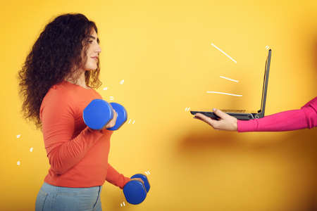 Girl with handlebars ready to start the gym online with a computer. yellow background