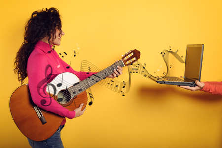 Happy woman follows a guitar lesson online. Yellow backgroundの写真素材