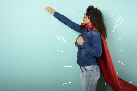 Woman acts like a superhero. Concept of determination and power. Cyan backgroundの写真素材