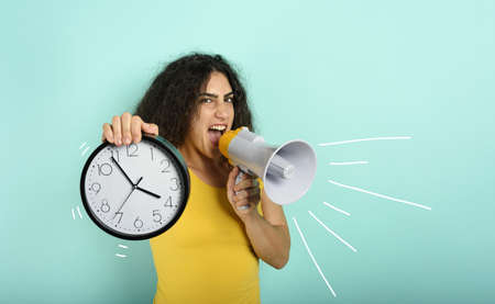Woman screams with loudspeaker because is too late. angry expression. cyan background