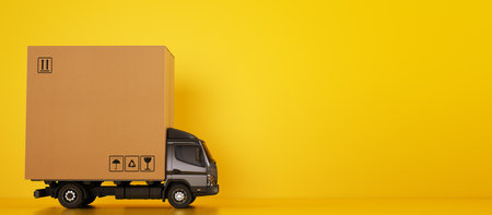 Big cardboard box package on a grey truck ready to be delivered on yellow backgroundの写真素材