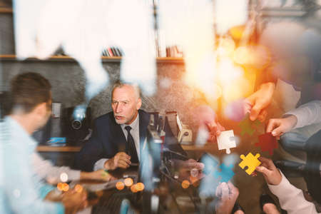 Business people join puzzle pieces in office. Concept of teamwork and partnership. double exposure with light effectsの写真素材