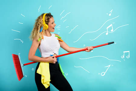 Funny housewife use broom like a rock guitar. cyan backgroundの写真素材