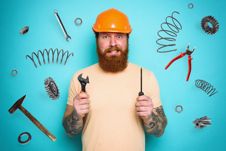 Confused man with screwdriver and spanners. worried and uncertain expression. cyan backgroundの写真素材