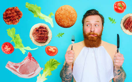 Man with tattoos is ready to eat with cutlery in hand. cyan backgroundの写真素材