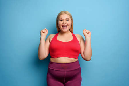 Fat girl does gym at home. satisfied and successfully expression. cyan background.