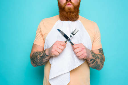 Man with tattoos is ready to eat with cutlery in hand