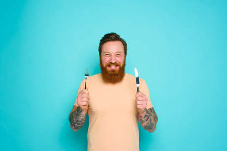 Happy man with tattoos is ready to eat with cutlery in hand