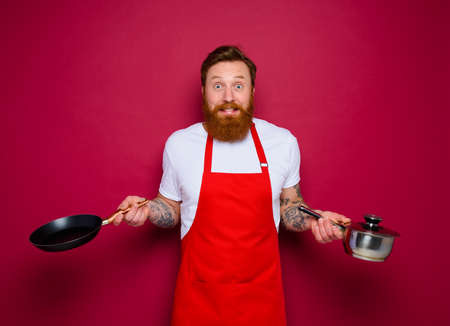 afraid chef with beard and red apron cooks with pan and potの写真素材