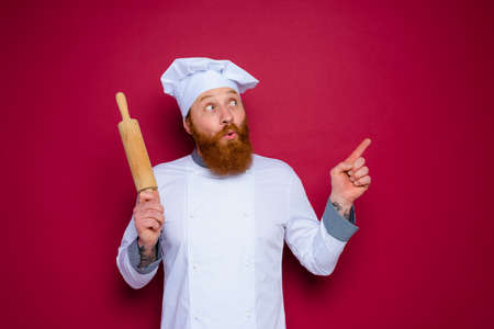 amazed chef with beard and red apron chef holds wooden rolling pinの写真素材