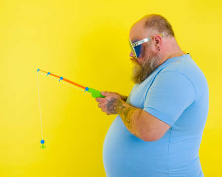 Fat man with beard and sunglasses is unhappy with the fishing rodの写真素材