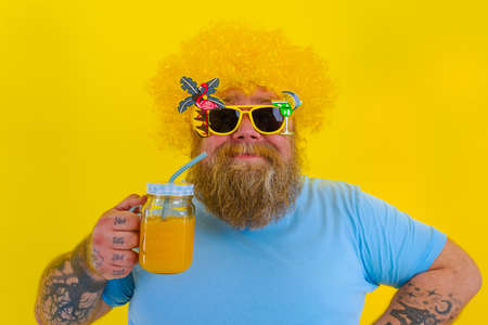 Fat happy man with wig in head and sunglasses drinks a fruit juiceの写真素材
