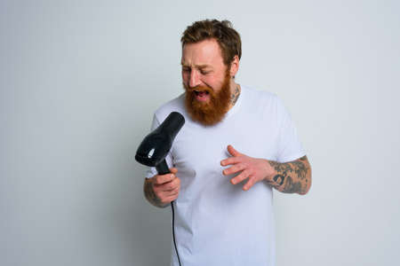 Happy man with beard use hair dryer as microphone and dancesの写真素材