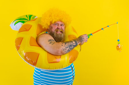 Fat happy man with wig in head plays with the fishing rodの写真素材
