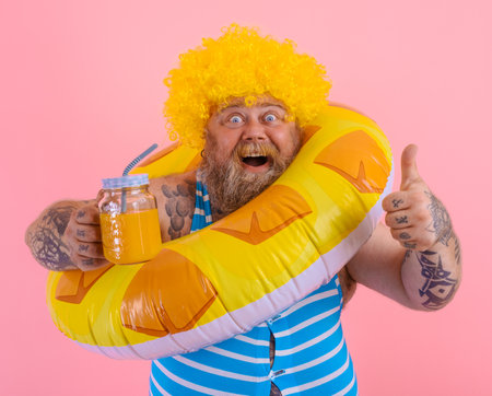 Fat happy man with wig in head is ready to swim with a donut lifesaverの写真素材