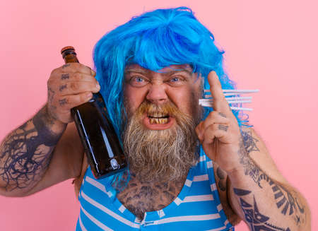 Fat man with beard and wig smokes cigarettes and drinks beerの写真素材