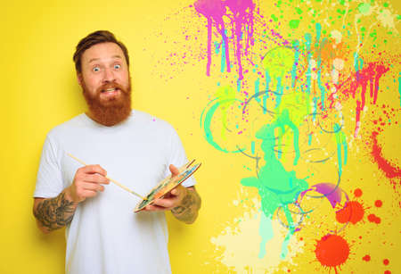 Doubter man with beard and tattoo is ready to draw with brushesの写真素材