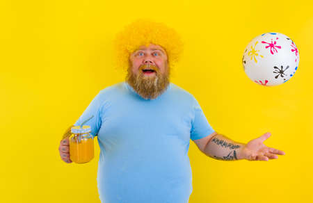 Fat happy happy man with wig in head and sunglasses drinks a fruit juiceの写真素材
