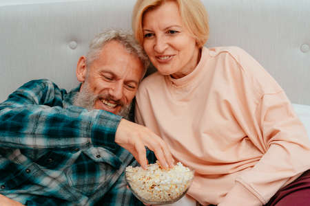 Husband and wife watch a film on the bed and eat popcornの写真素材