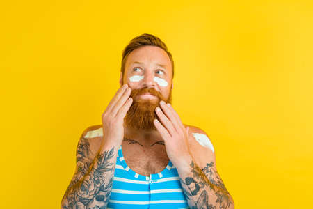 man with tattoos and swimsuit puts on sunscreen