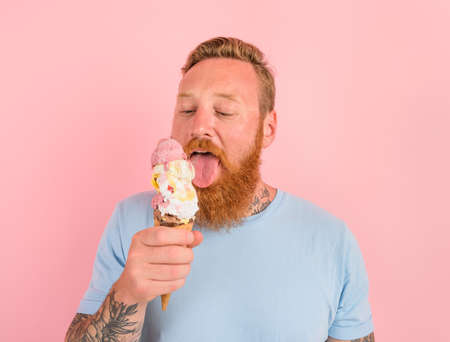 Hungry man with beard and tattoos eats a big icecream