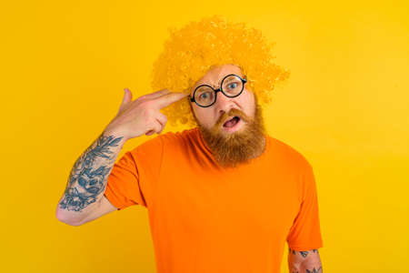 man with beard, yellow wig and glasses does a gun gesture with the handの写真素材