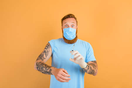 Afraid man with beard, tattoo and mask for covid-19 is ready for the virus vaccineの写真素材
