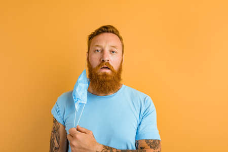 man with beard and tattoos removes the mask for covid-19