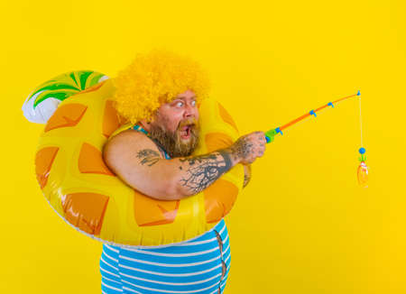 Fat amazed man with wig in head plays with the fishing rodの写真素材