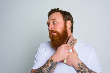 Serious man with blade is focused on cutting his beardの写真素材