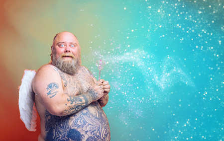 Fat amazed man with beard ,tattoos and wings acts like an magic fairyの写真素材
