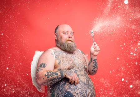Fat thoughtful man with beard ,tattoos and wings acts like an magic fairyの写真素材