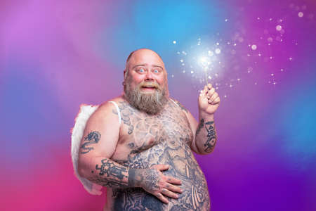 Fat happy man with beard ,tattoos and wings acts like an magic fairyの写真素材
