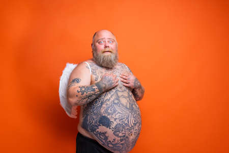 Fat amazed man with beard ,tattoos and wings acts like an angelの写真素材
