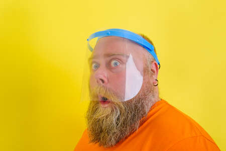 Amazed man with beard and tattoos wears a protective face shield against covid-19の写真素材
