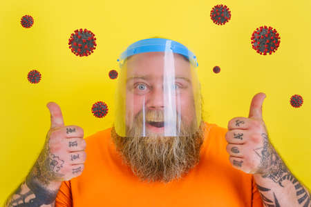 Happy man with beard and tattoos wears a protective face shield against covid-19の写真素材