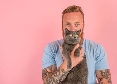 Man with beard and tattoos caresses a grey catの写真素材