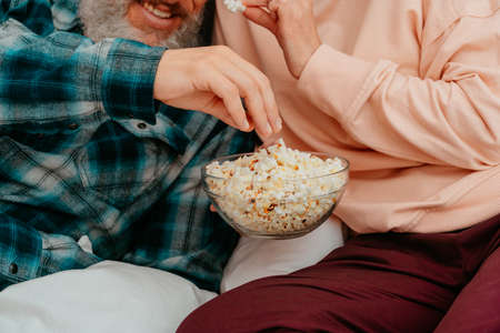 Husband and wife watch a film on the bed and eat popcornの写真素材